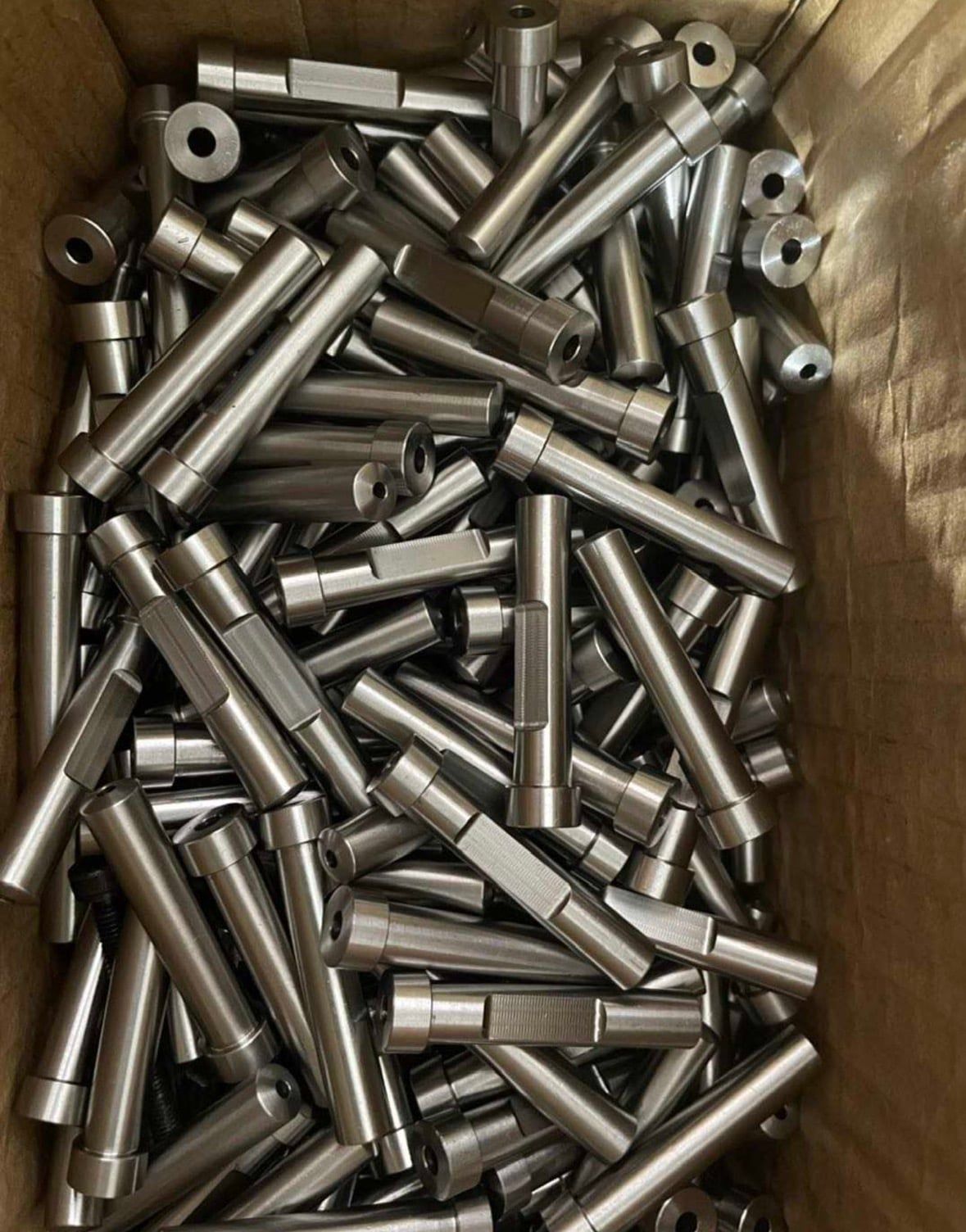 A bin of steel standoffs with cross-holes and machined flats